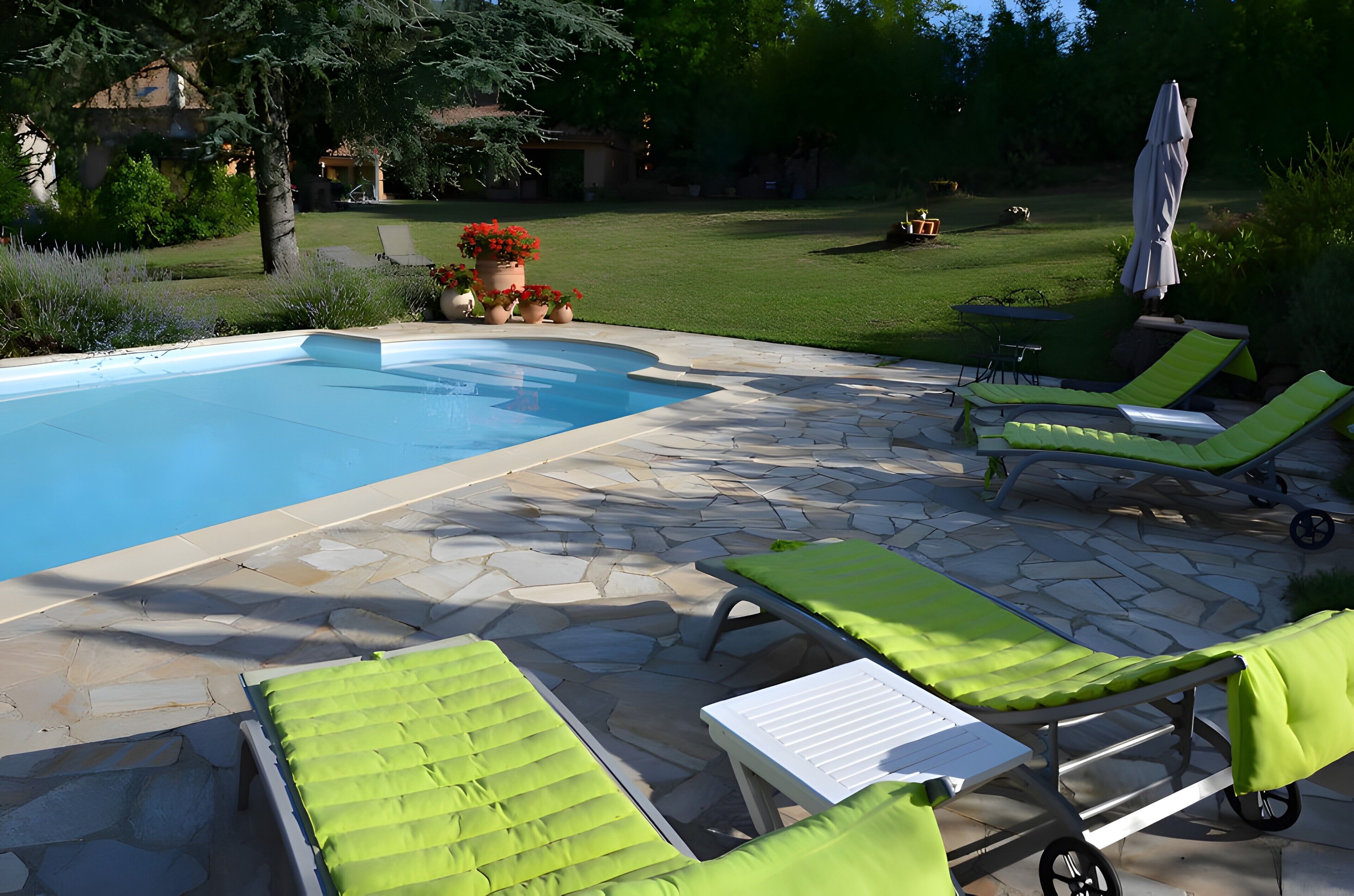 Una piscina con baldosas de piedra, sillas de descanso verdes y un césped.