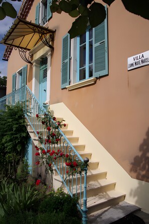 A building with a sign reading 'VILLA JEANNE MARIE MARCELLE,' a staircase with blue railings, and red flowers.