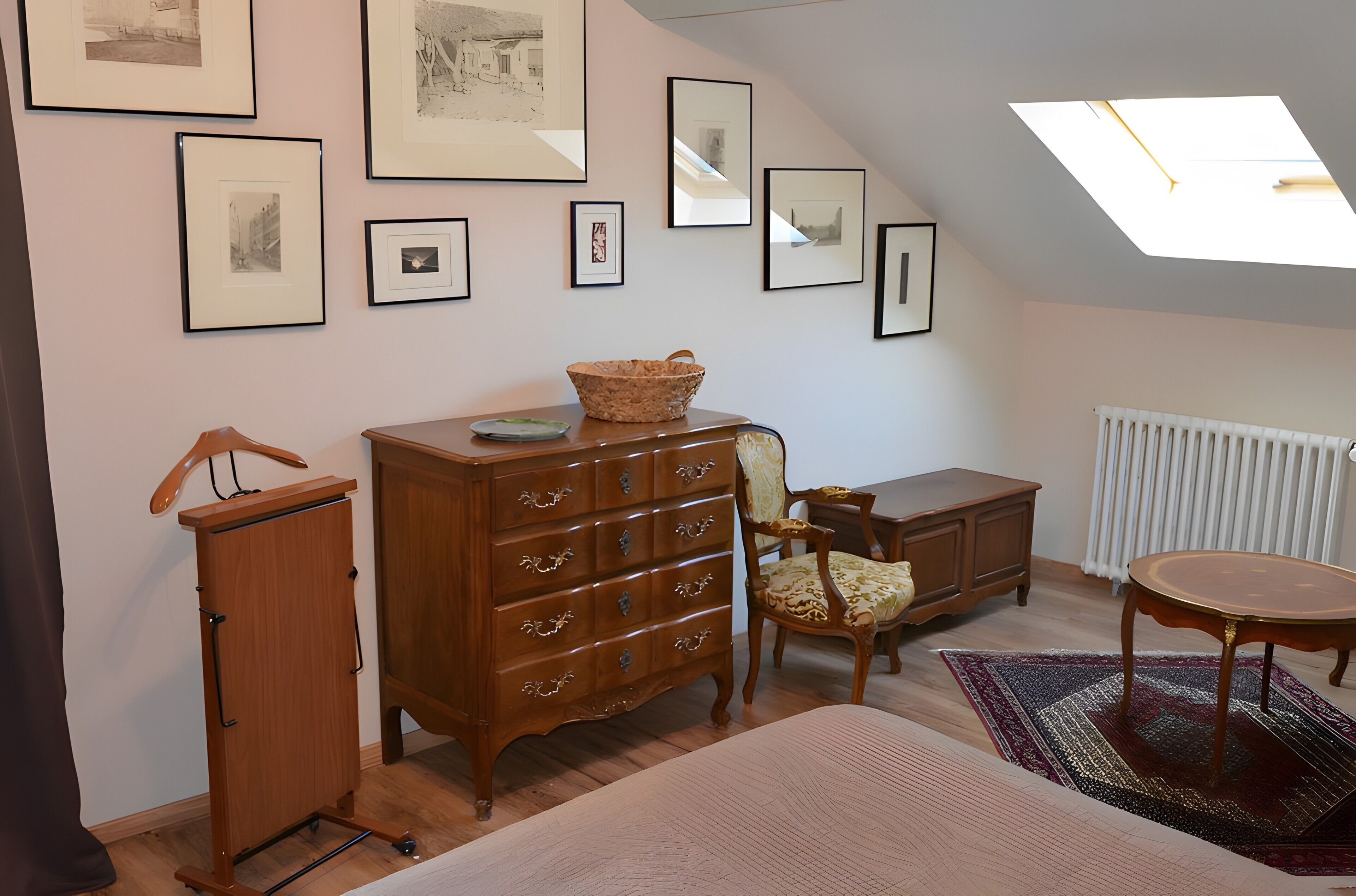 Une pièce comprenant un lit, une commode, une chaise, une table et des tableaux encadrés accrochés au mur.