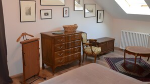 A room with a bed, dresser, chair, table, and framed pictures on the wall.