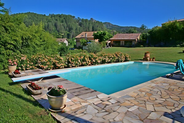 Uma piscina com ladrilhos de pedra, rodeada por um jardim com diversas plantas e flores.