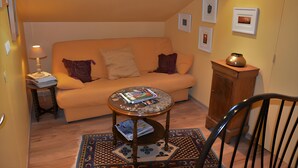 A cozy living room with a sofa, a coffee table, a lamp, and a chair. There are framed pictures on the wall and a vase on a cabinet.