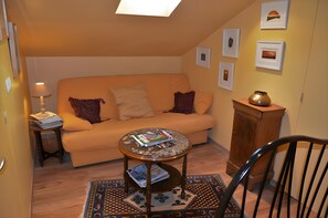 A cozy living room with a sofa, a coffee table, a lamp, and a chair. There are framed pictures on the wall and a vase on a cabinet. - Guest Room in Family Home – The Engraving Room at the Foot of the Monts d'Ardèche (Jaujac)