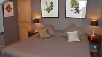 A bedroom with a bed, two bedside tables with lamps, a door, and two framed botanical prints on the wall.