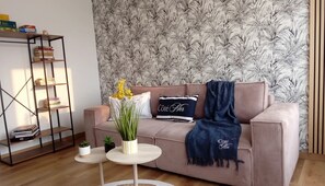 Ein Wohnzimmer mit einer Couch, einem kleinen Tisch, einem Bücherregal und einer gemusterten Tapete.