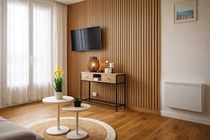 Ein modernes Wohnzimmer mit Flachbildfernseher, Holzpaneele, einem kleinen runden Tisch mit Pflanze und einer Couch.