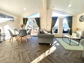 A spacious living area with a sofa, dining table, chairs, and a view through large windows. - 2 Bed in Honiton (oc-76515) (Fenny Bridges)