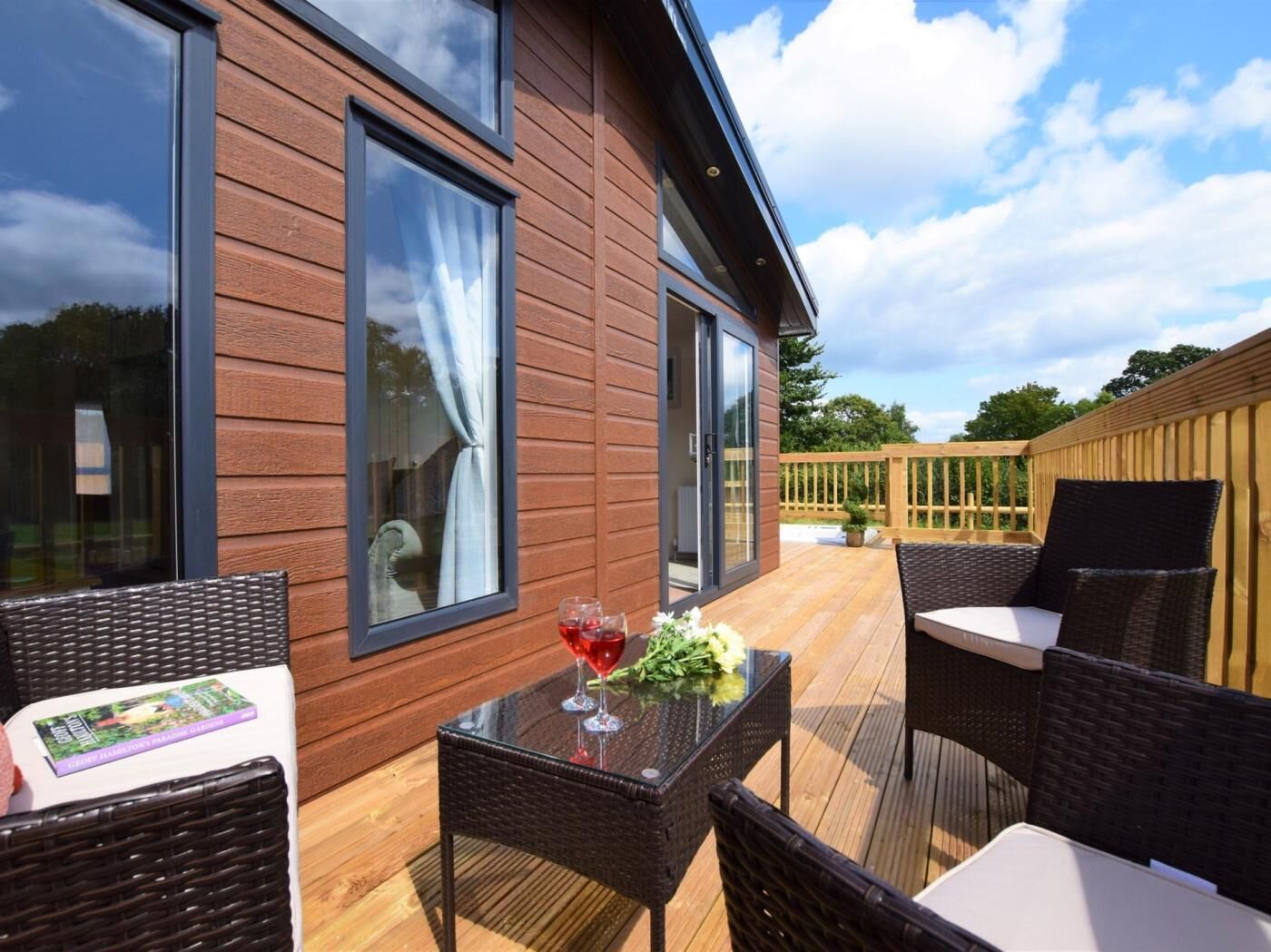 Une terrasse en bois aménagée avec du mobilier d’extérieur, notamment des fauteuils en osier et une table avec un plateau en verre.