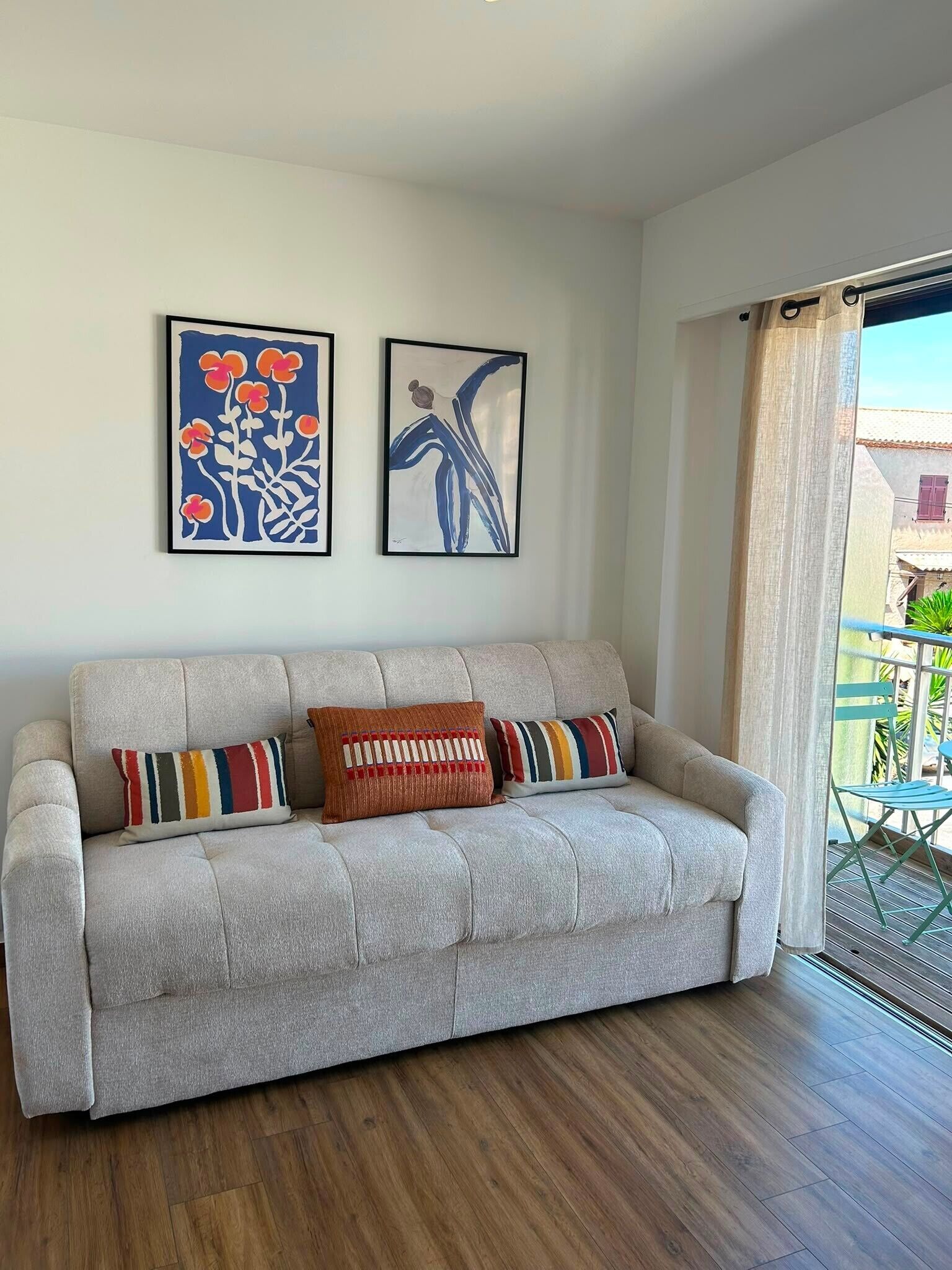 A living room with a grey sofa, two framed artworks, and a wooden floor.