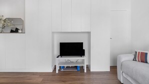 Una sala moderna con un mueble blanco para equipo de entretenimiento, un televisor de pantalla plana y un sofá con un cojín a rayas.