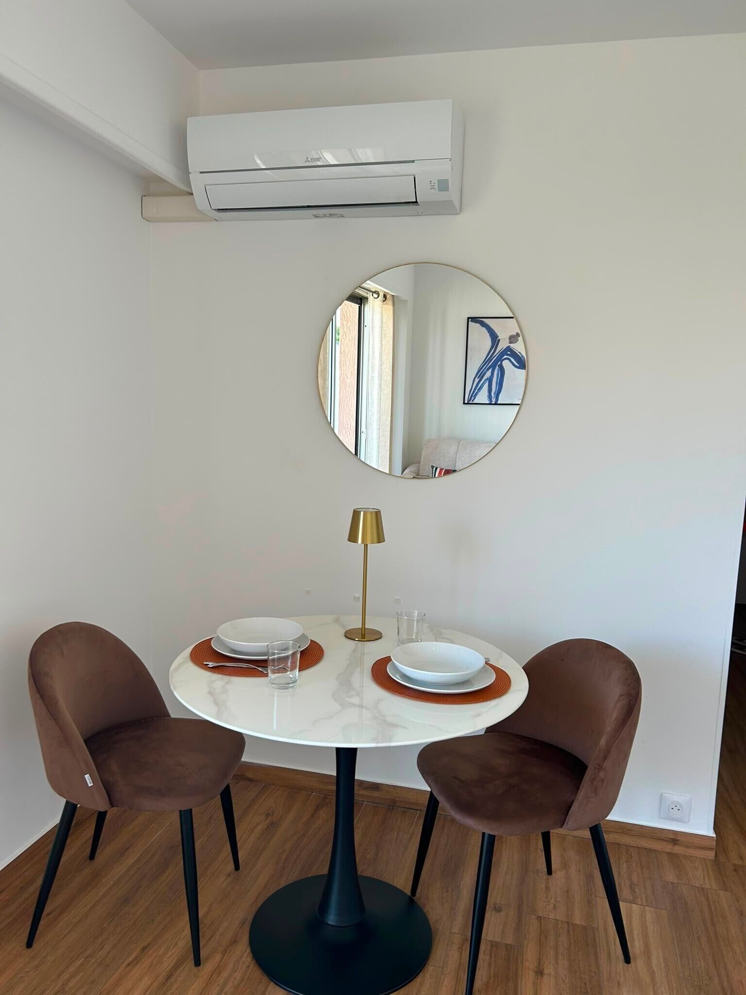 Un coin repas comprenant une table ronde, deux chaises, un miroir et un appareil de climatisation installé au-dessus.
