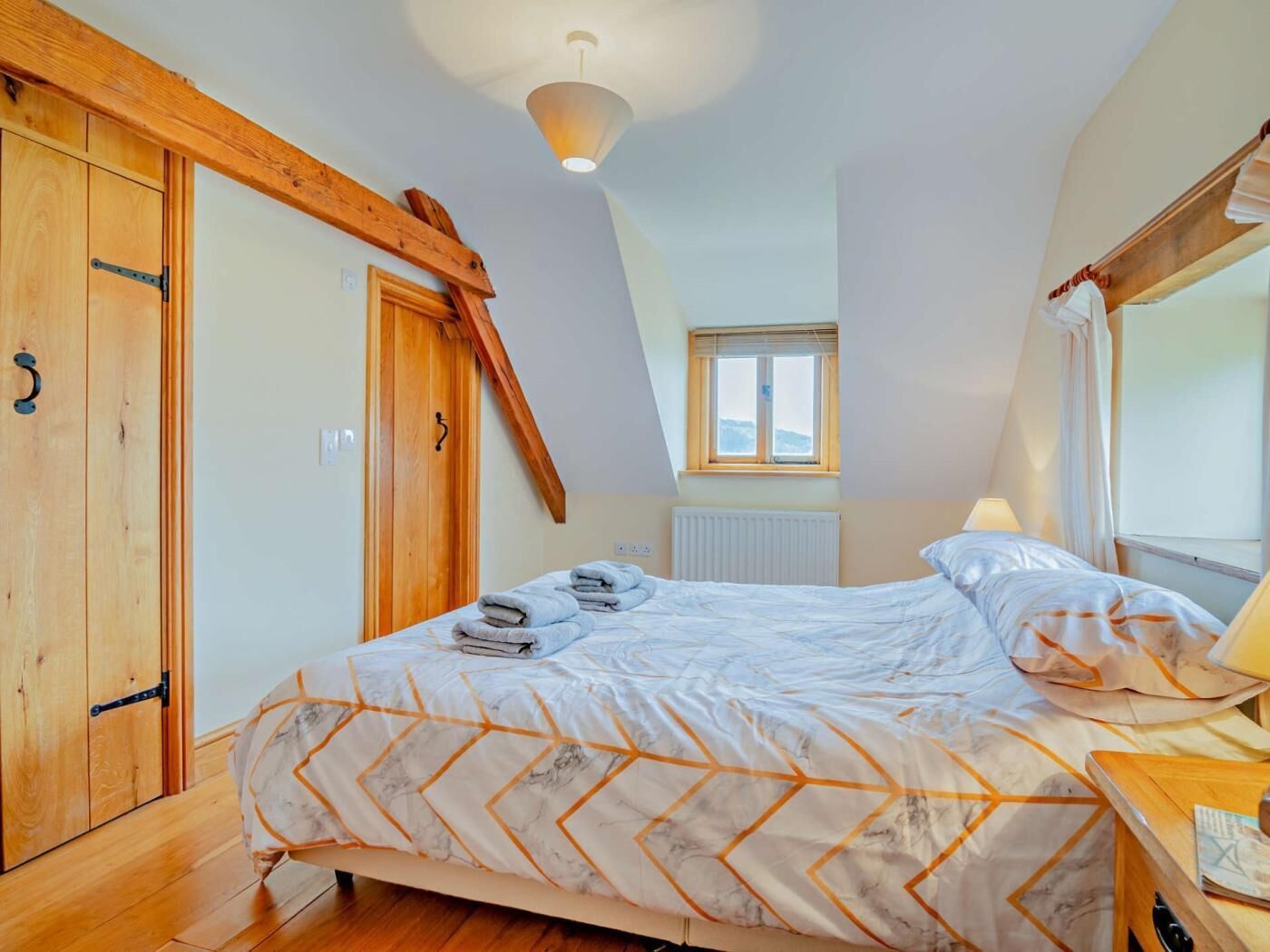 A bedroom with a bed, a wooden wardrobe, a window, and a ceiling light.