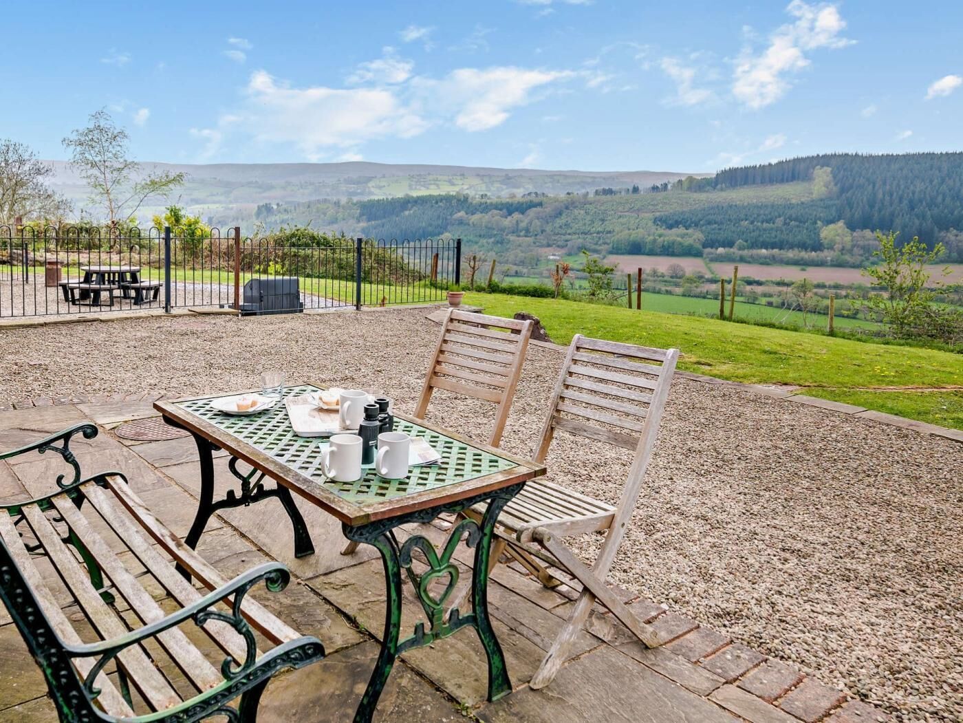 Een terras met een tafel en stoelen, een uitzicht op het landschap en een hek op de achtergrond.