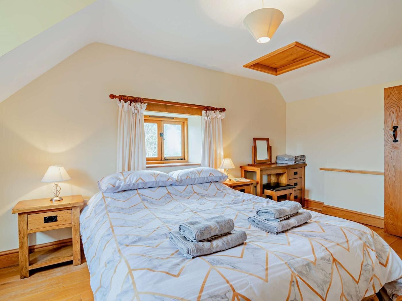 A bedroom with a bed, bedside tables, a window, a mirror, and a wardrobe.