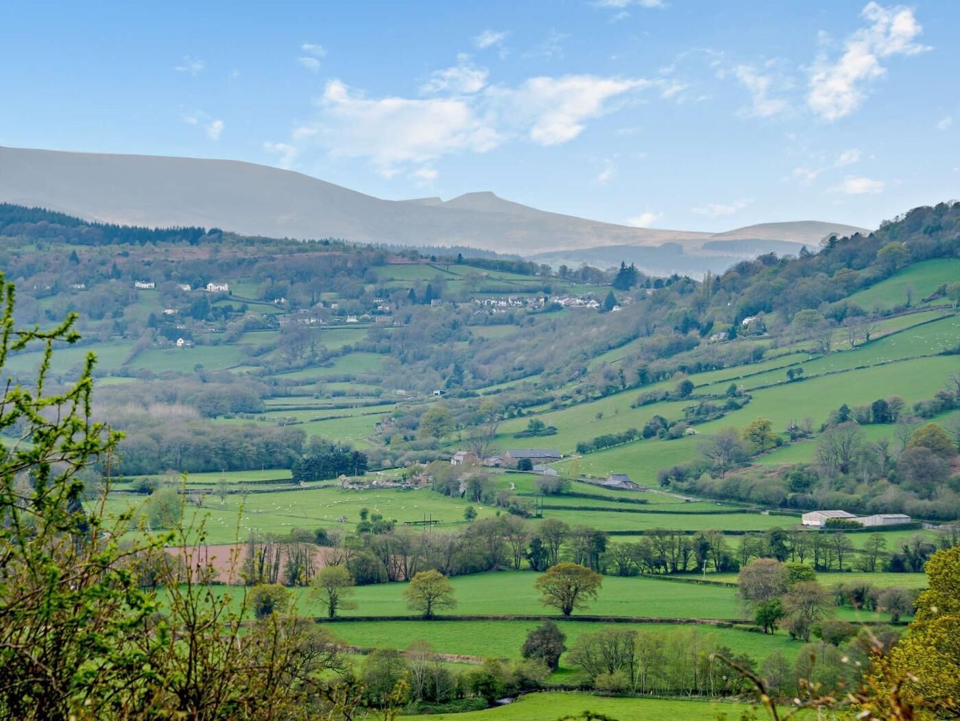 A rural landscape with rolling hills, scattered houses, and fields.