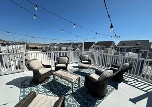 Ein Balkon mit Korbmöbeln, einem gemusterten Teppich und Lichterketten.