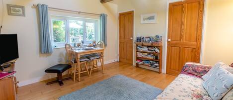 A cozy room with a wooden dining table, chairs, a bookshelf, a sofa, and a television.