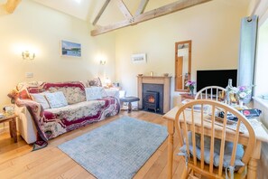 A cozy living room with a fireplace, a sofa, a dining table with chairs, and a TV. - 1 Bed in Falmouth (oc-85594) (Brill)