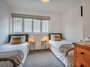 A bedroom with two beds, a window with blinds, bedside lamps, a radiator, and a wooden dresser. - 2 Bed in Flamborough (oc-g0115) (Flamborough)