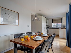 A modern kitchen with white cabinets, a dining table set with plates, glasses, and a fruit bowl. - 2 Bed in Flamborough (oc-g0115) (Flamborough)