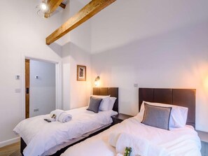 Ett hotellrum med två sängar, en synlig takbalk i trä, en väggmonterad lampa och en dörr.