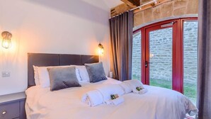 Ein Schlafzimmer mit Bett, Nachttisch, Wandleuchten und einer roten Tür zu einer Steinsäule.