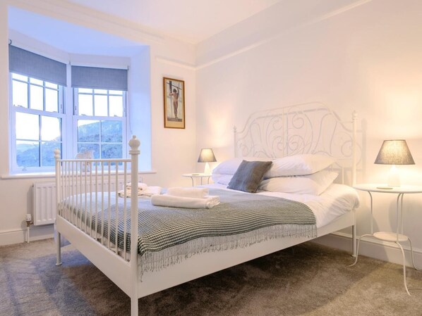 Una cama con dosel blanco con una colcha a cuadros, dos lámparas de noche y una ventana con vistas a una montaña.