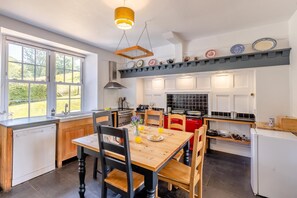A modern kitchen with a dining area, large windows, and a view of the outdoors.