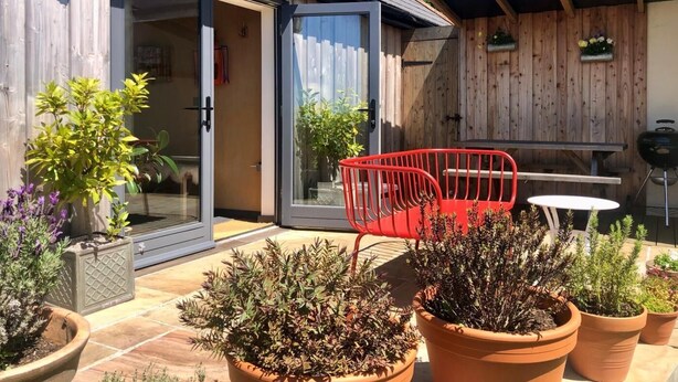En terrasse med plantekasser, en rød stol og et bord.