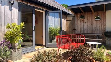 Une terrasse agrémentée de plantes en pot, d’une chaise rouge et d’une table.