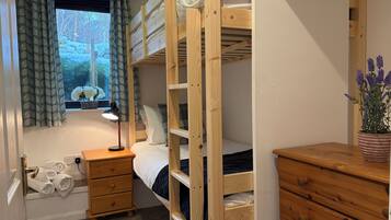 Een slaapkamer met stapelbed, raam, bedlamp, houten dressoir en spiegel.