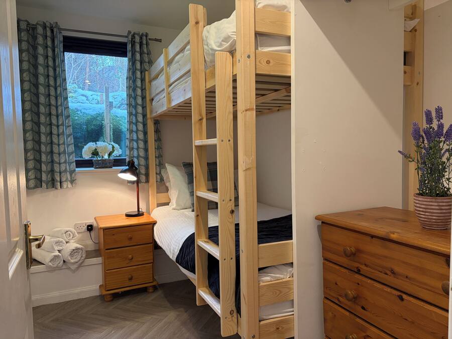 Een slaapkamer met stapelbed, raam, bedlamp, houten dressoir en spiegel.