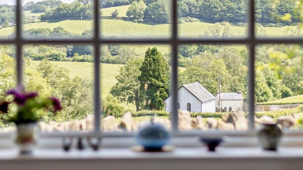 A view through a window with a rural landscape, including a white building and trees. - 1 Bed in Brecon (oc-bn129) (Yscir)