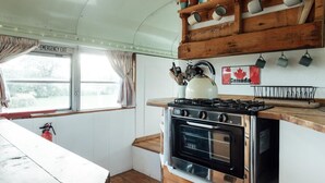A compact kitchen with a stove, oven, and wooden shelves above. - 1 Bed in Axminster (oc-82585) (Musbury)
