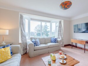 Ein Wohnzimmer mit einer Couch, einem Couchtisch mit Gegenständen, einer Lampe und einem Fernseher an der Wand.