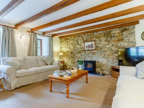 A cozy living room with a stone wall, a fireplace, a sofa, a coffee table, and a TV. - 2 Bed in St. Austell (oc-82609) (Pentewan Valley)