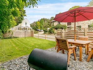 A patio with a grill, wooden table, chairs, and a red umbrella. - 2 Bed in St. Austell (oc-82609) (Pentewan Valley)