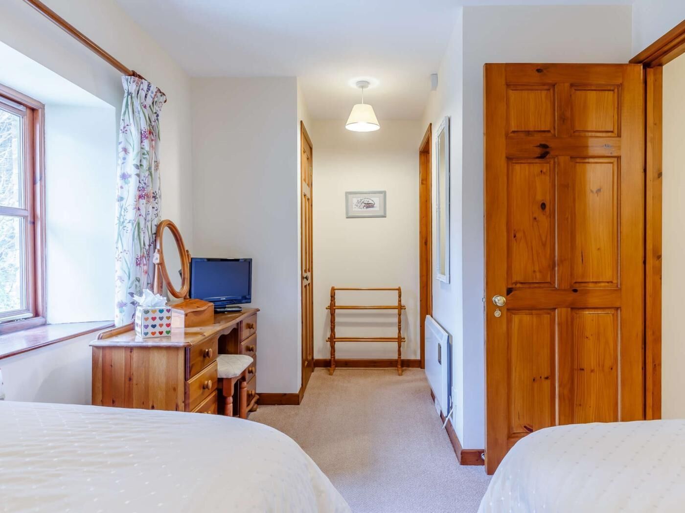 Une chambre avec deux lits, un bureau avec un ordinateur, un miroir et une fenêtre avec des rideaux.