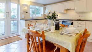 A kitchen with a dining table set for four, a coffee maker, and a vase with flowers. - 2 Bed in Holt (oc-ncc11) (Holt)