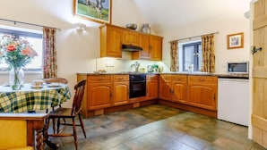 A kitchen with wooden cabinets, a dining table with a checkered tablecloth, and a vase of flowers. - 1 Bed in Leighton (oc-80726) (Leighton)