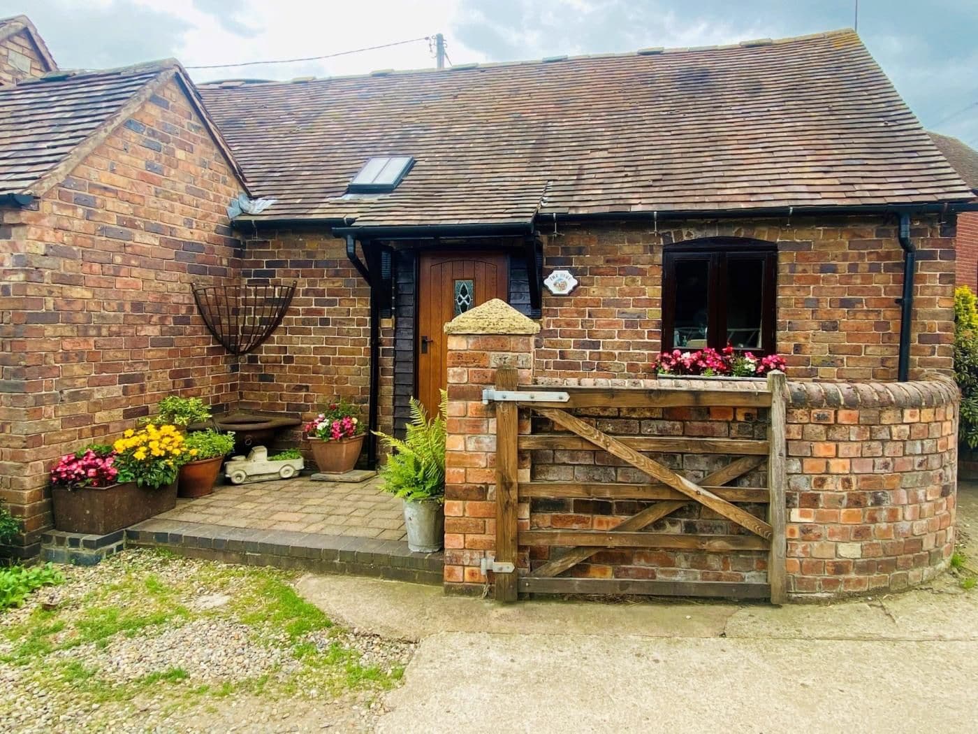 A brick house with a wooden gate, a small porch with potted plants, and a visible chimney.