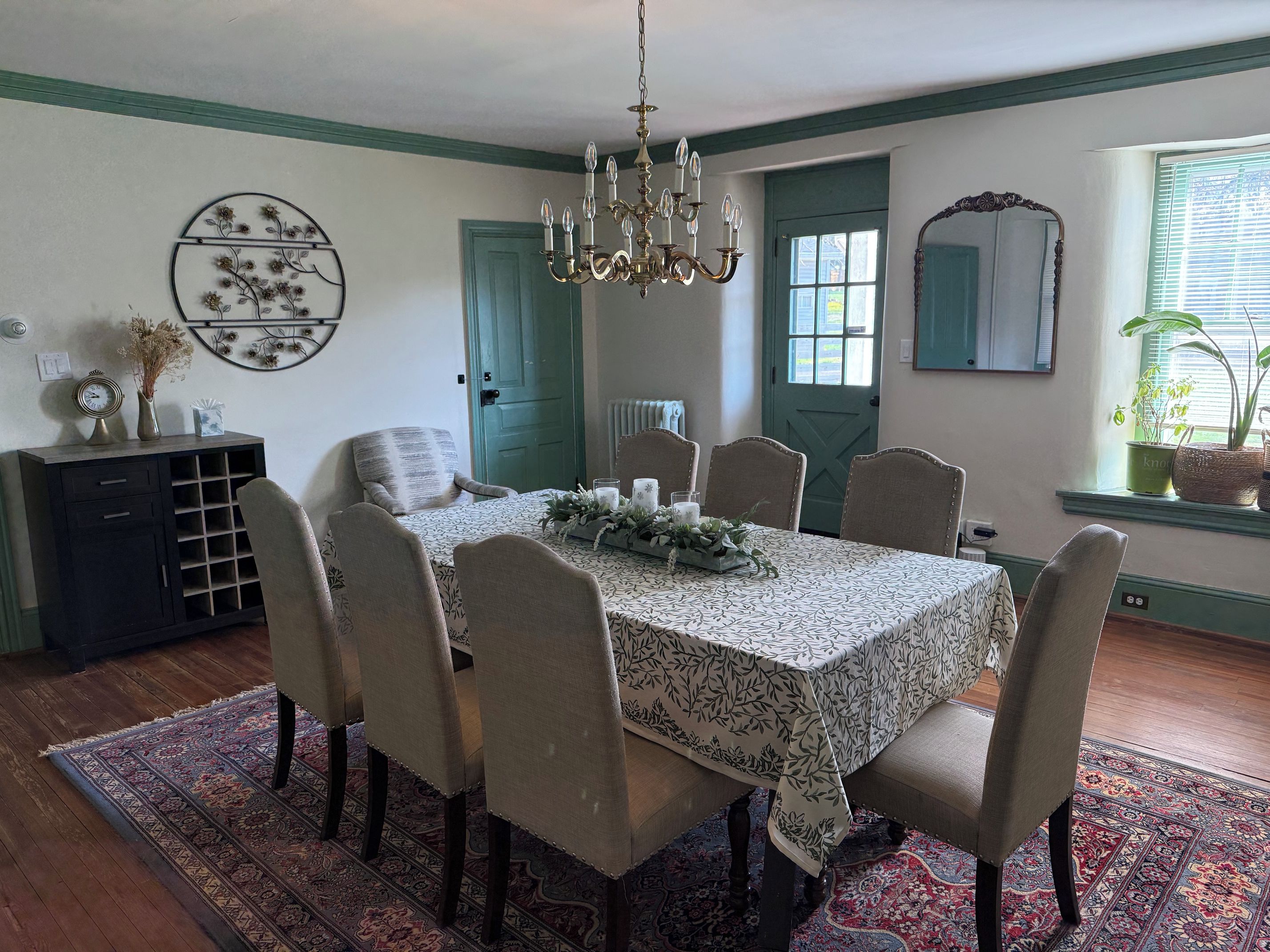 A dining room with a table set for six, surrounded by six chairs, a chandelier, and a decorative wall piece.