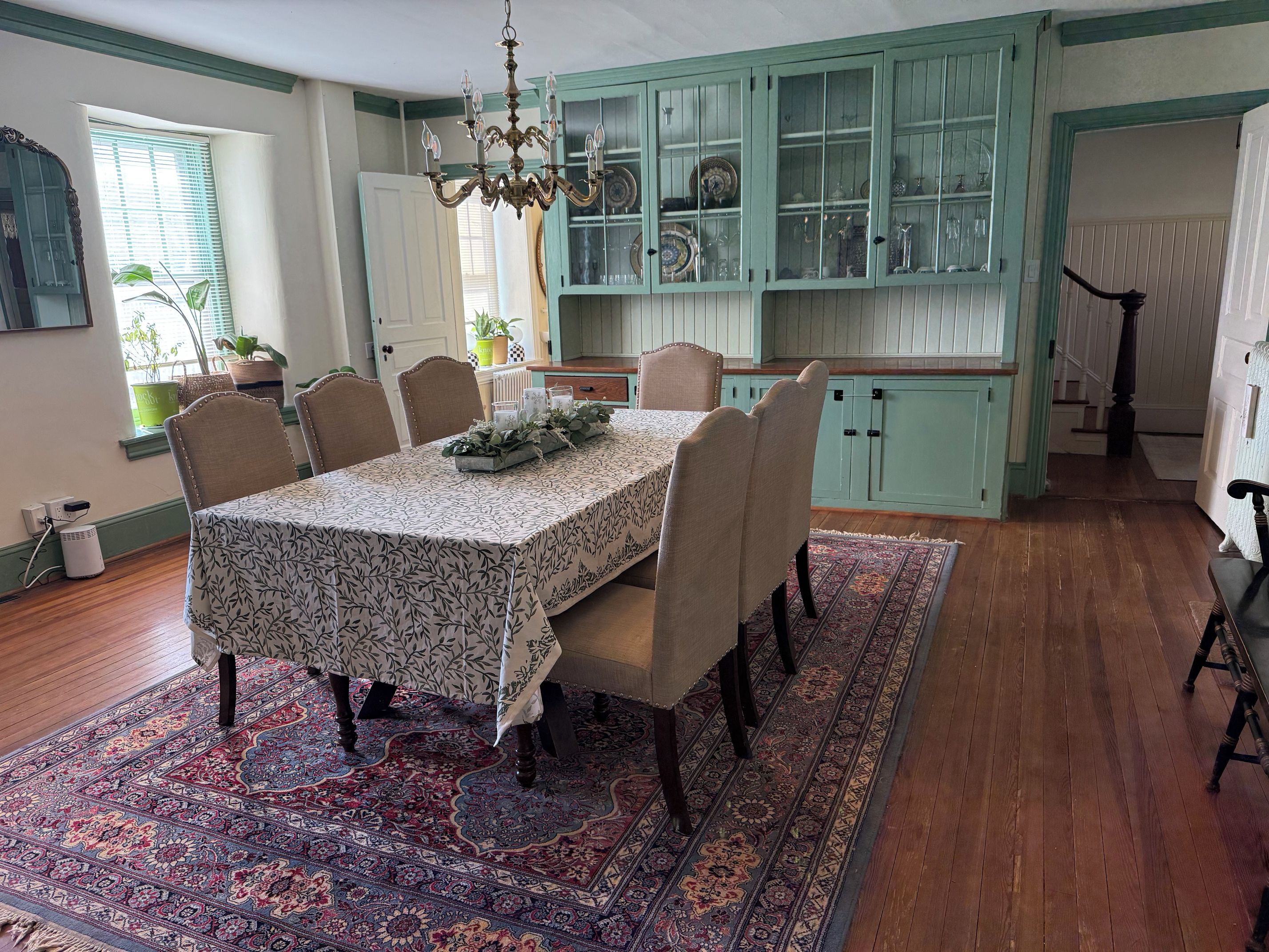 A dining area with a table set for four, surrounded by chairs, a patterned rug, and a chandelier.