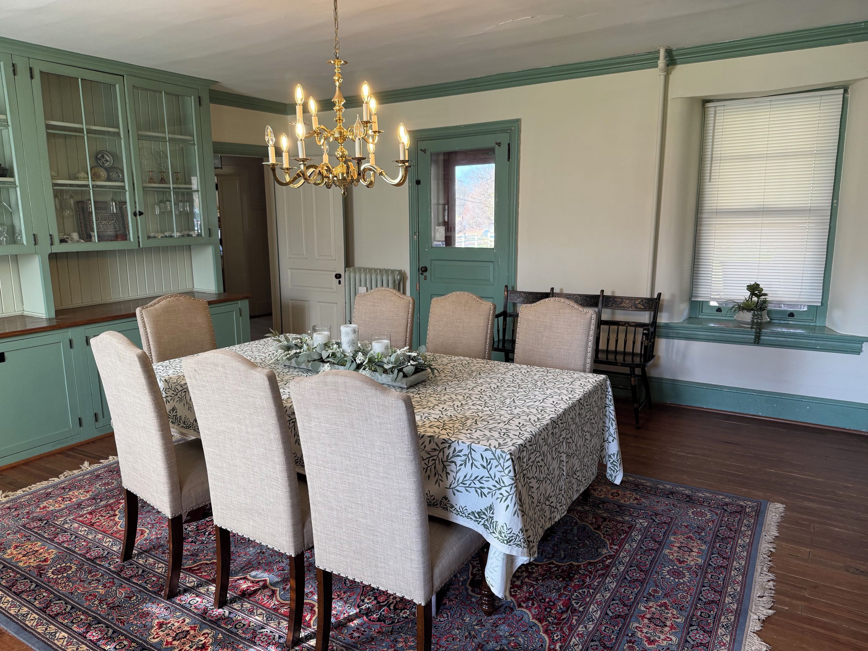A dining room with a table set for six, surrounded by chairs, a chandelier, and a patterned rug.