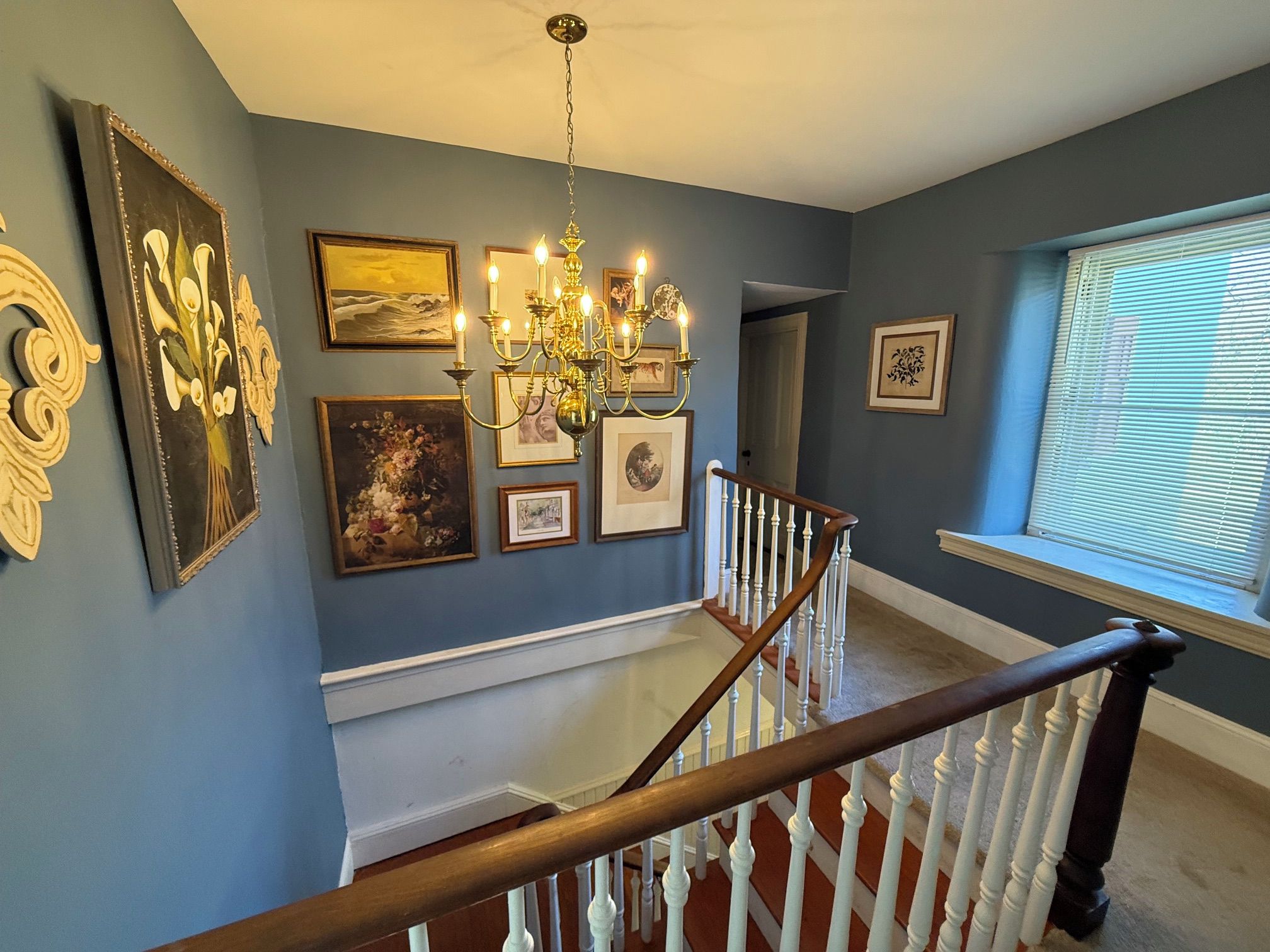 A staircase with white balusters leading to a landing with a chandelier and framed artwork.