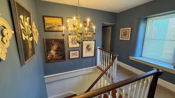 A staircase with white balusters leading to a landing with a chandelier and framed artwork.