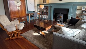 Un salon avec une cheminée, un meuble en bois, un bureau, une bibliothèque et une horloge au mur.