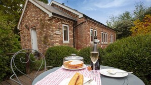 A table with a checkered tablecloth, a bottle of wine, a covered cake, and a sandwich on a patio with a brick building in the background. - 1 Bed in Howden (oc-g0181) (Saltmarshe)