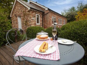 A table with a checkered tablecloth, a bottle of wine, a covered cake, and a sandwich on a patio with a brick building in the background. - 1 Bed in Howden (oc-g0181) (Saltmarshe)