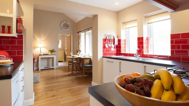 A kitchen with a wooden floor, a dining area with a table and chairs, a fruit bowl on the counter, and a clock on the wall. - 1 Bed in Howden (oc-g0181) (Saltmarshe)